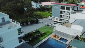 A modern hotel with a rooftop pool, outdoor seating, and a lush green lawn.