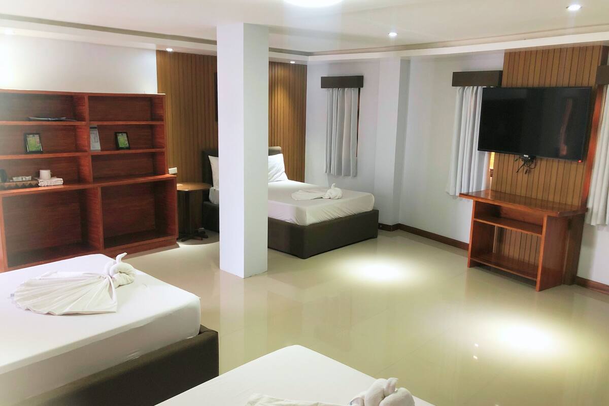 Quarto de hotel com uma cama, televisão, prateleira de madeira e mesa de cabeceira.