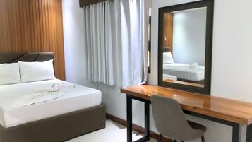 Habitación de hotel con cama, escritorio, silla, espejo grande y ventana con cortinas.