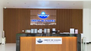 A reception desk at Orient De Galera Beach Resort with a wooden backdrop and a logo above.