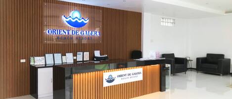 Mostrador de recepción en Orient De Galera Beach Resort con un fondo de madera y una señalización clara.