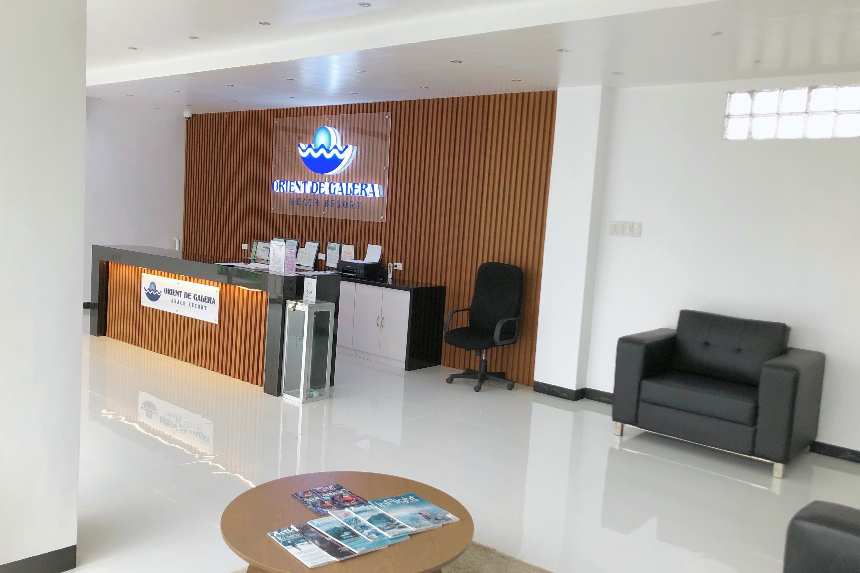 A reception area with a wooden panel wall, a reception desk, a black office chair, and a black sofa.