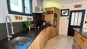 A modern kitchen with a curved countertop, a stainless steel sink, wooden cabinets, a built-in oven, and a 'BAR' sign on the wall. - Comfortable air-conditioned villa - private heated swimming pool 3 kms from Sarlat center (PROISSANS)
