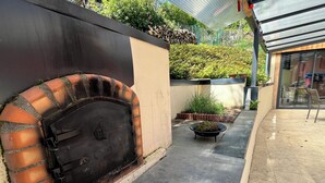 A brick oven in a courtyard with a paved walkway, surrounded by greenery and a building with a glass door. - Comfortable air-conditioned villa - private heated swimming pool 3 kms from Sarlat center (PROISSANS)