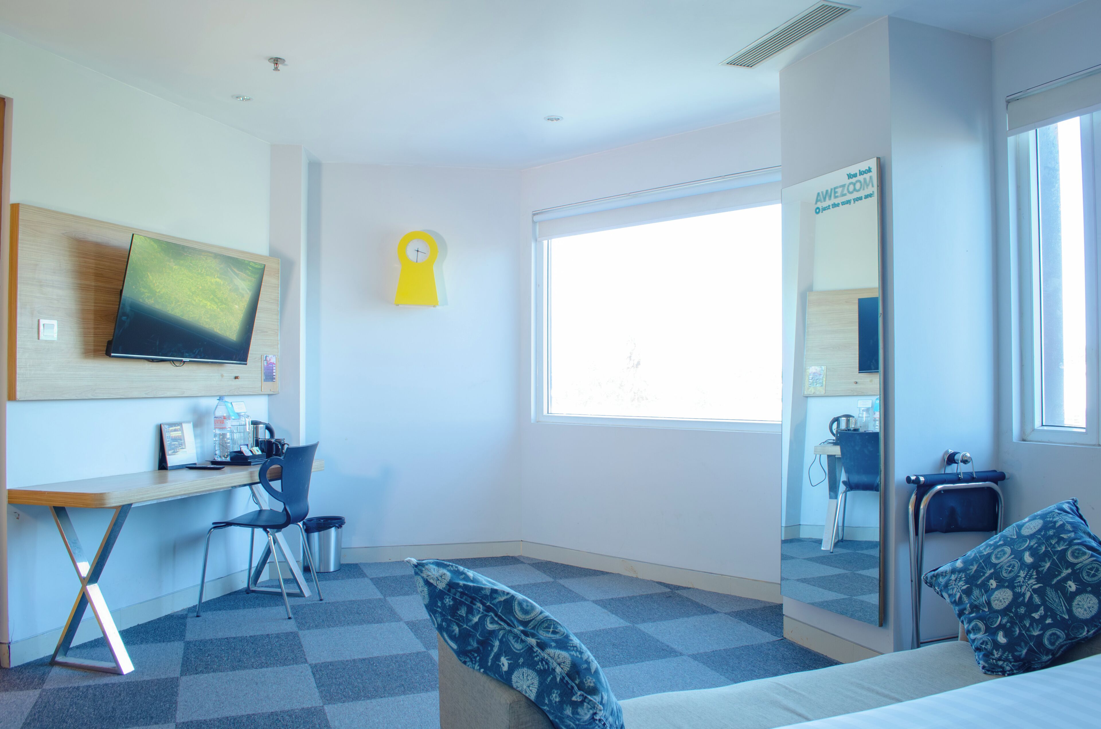 A hotel room with a desk, chair, bed, and a large window.