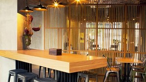 Een restaurantinterieur met een houten bar, zwarte krukken en een verticale houten scheiding.