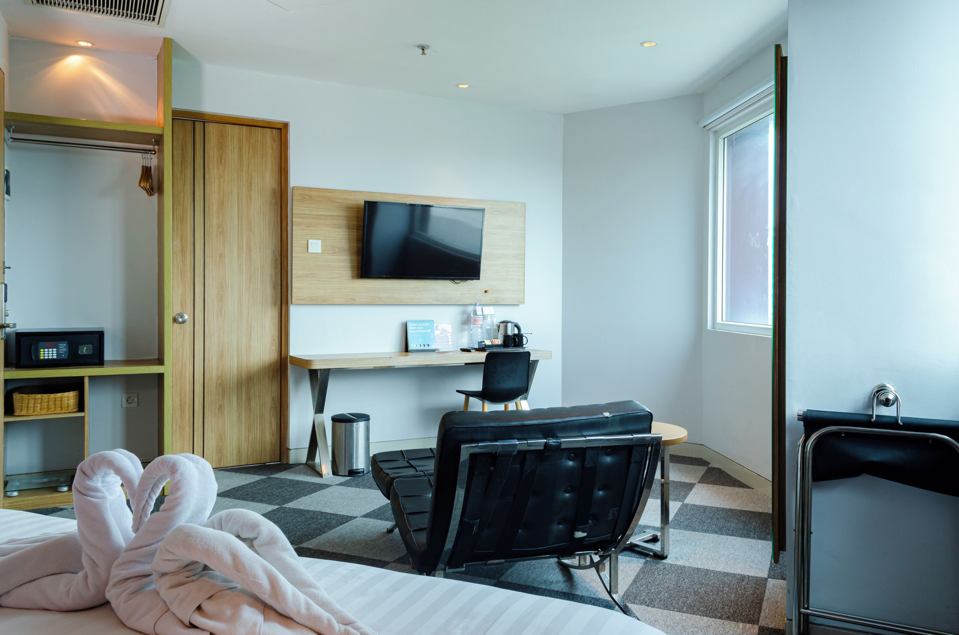 Habitación de hotel con cama, escritorio con silla, televisor montado en la pared, armario y ventana.