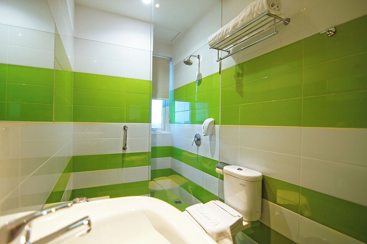 Een badkamer met groene en witte tegels, een badkuip, een toilet en een douche.