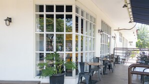 Een overdekt terras met tafels, stoelen, grote ramen en een potplant.
