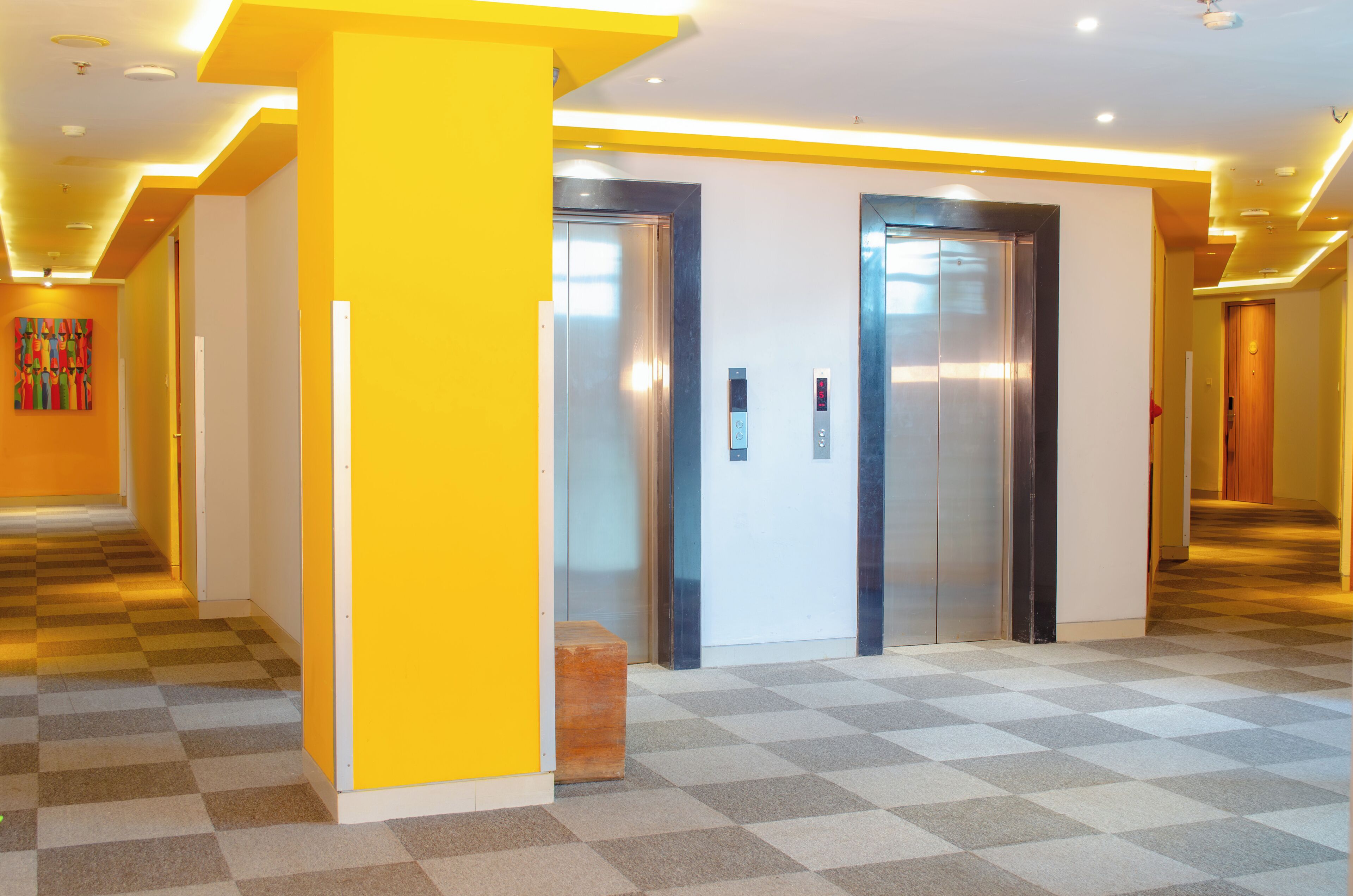 A hotel lobby with two elevators, a checkered floor, and a yellow accent wall.