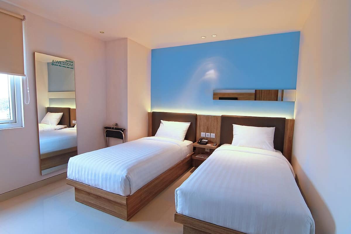 Habitació d'hotel amb dos llits, una taula de nit amb una làmpada, un mirall i una paret d'accent blava.