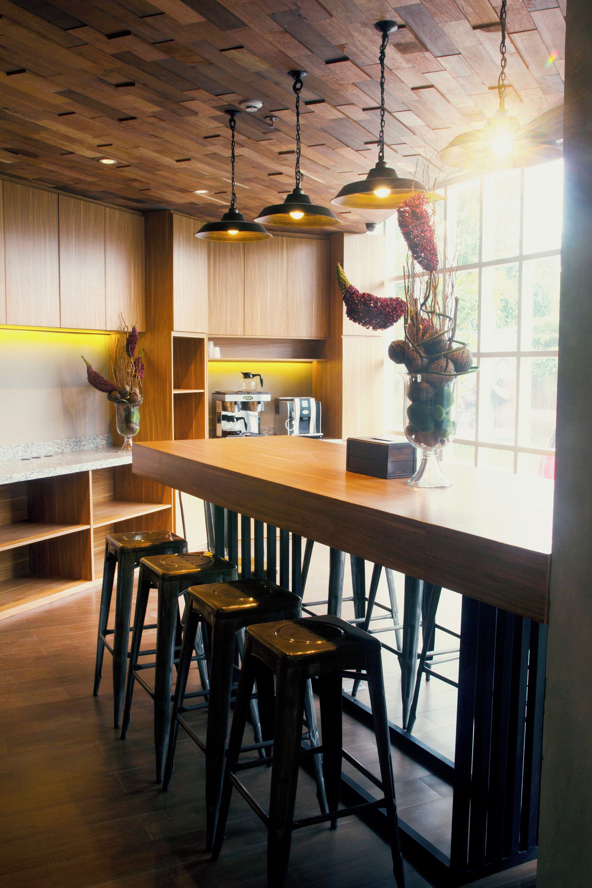 Eine moderne Küche mit Holzausstattung, einer Bar inklusive Barhocker und hängenden Pendelleuchten.