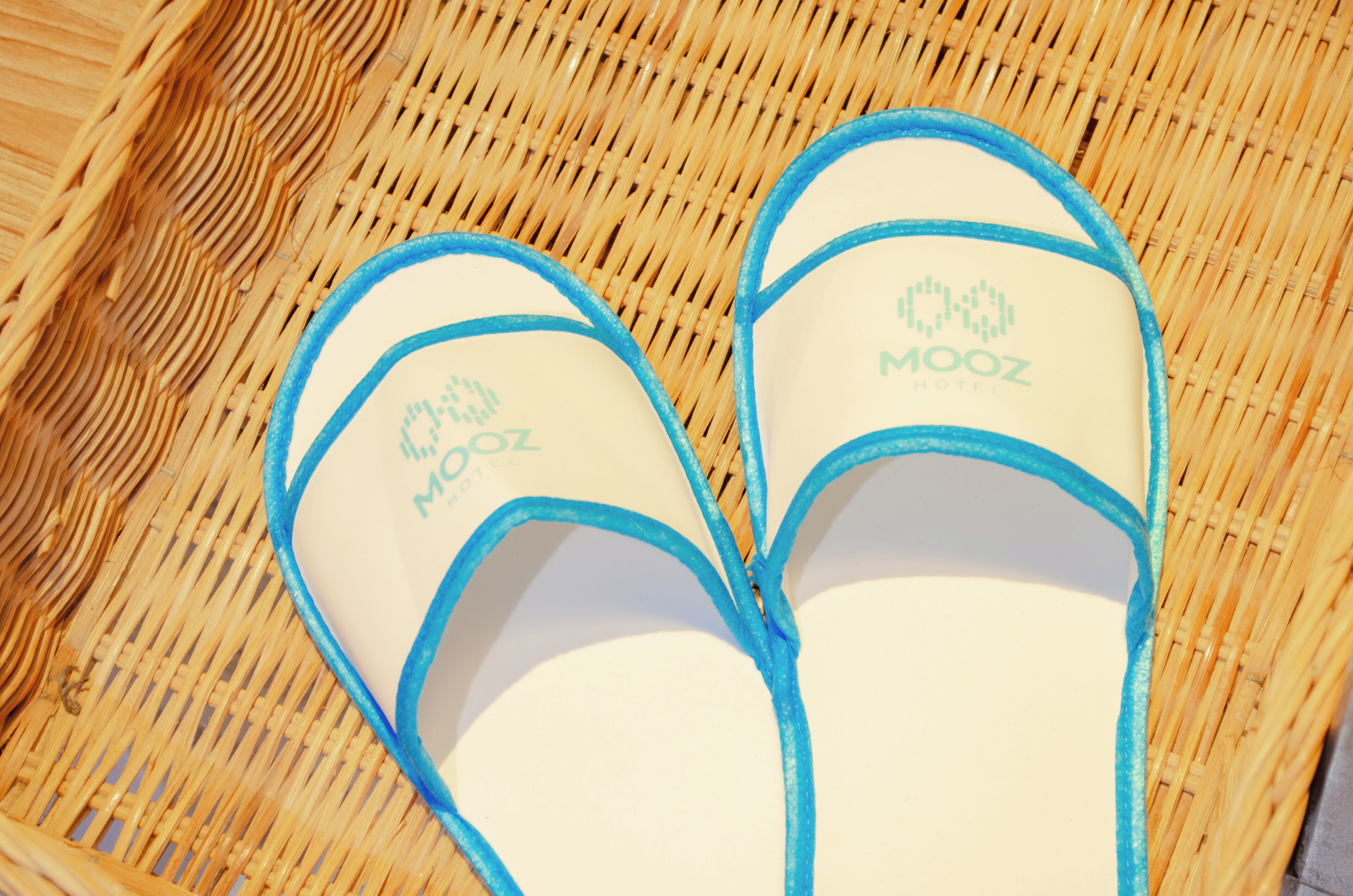 Hvide slippers med blå detaljer og 'MOOZ Hotel'-logo.