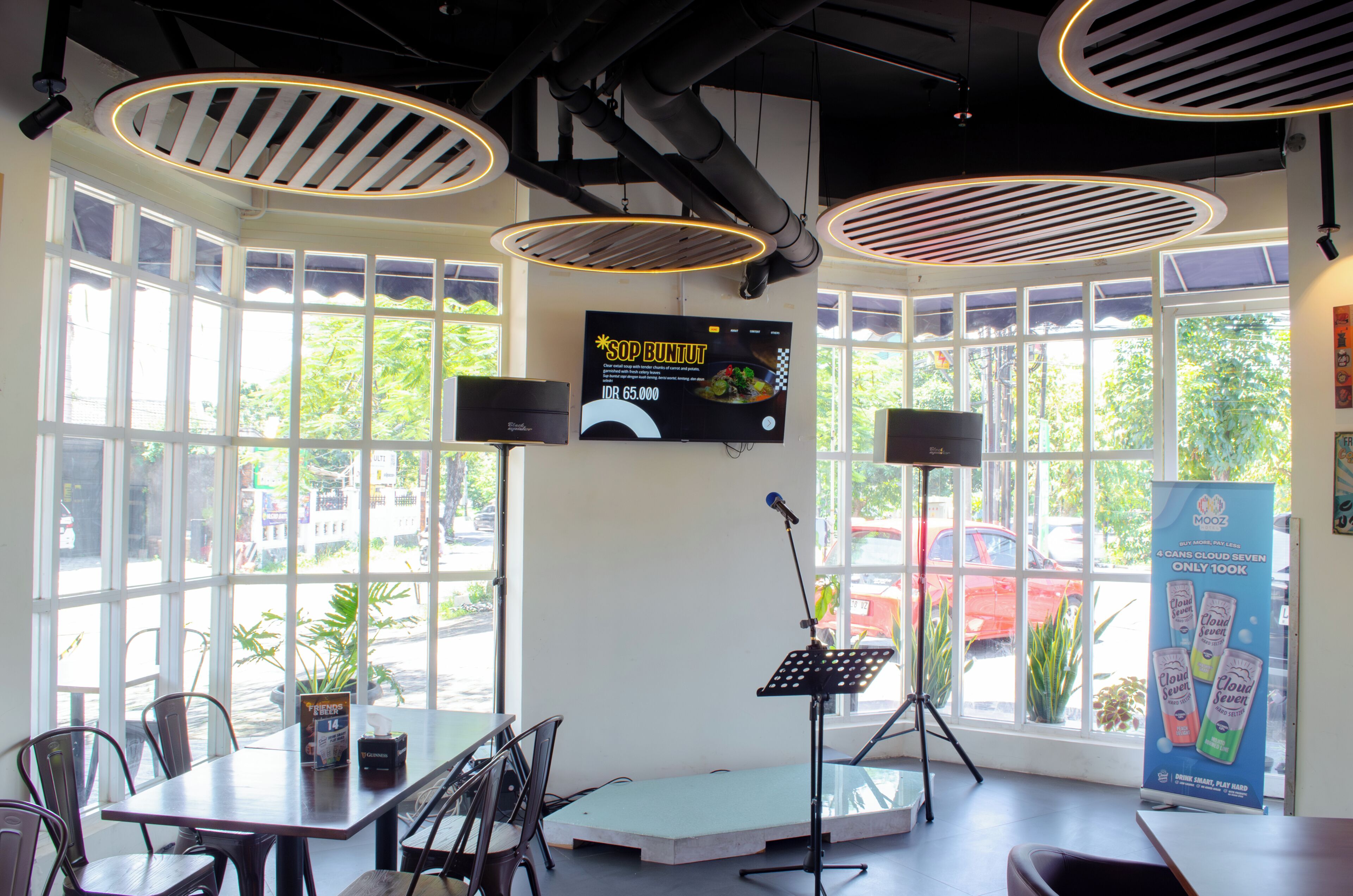 L’intérieur d’un restaurant, avec de grandes fenêtres, une scène équipée d’un microphone et un panneau affichant le menu.