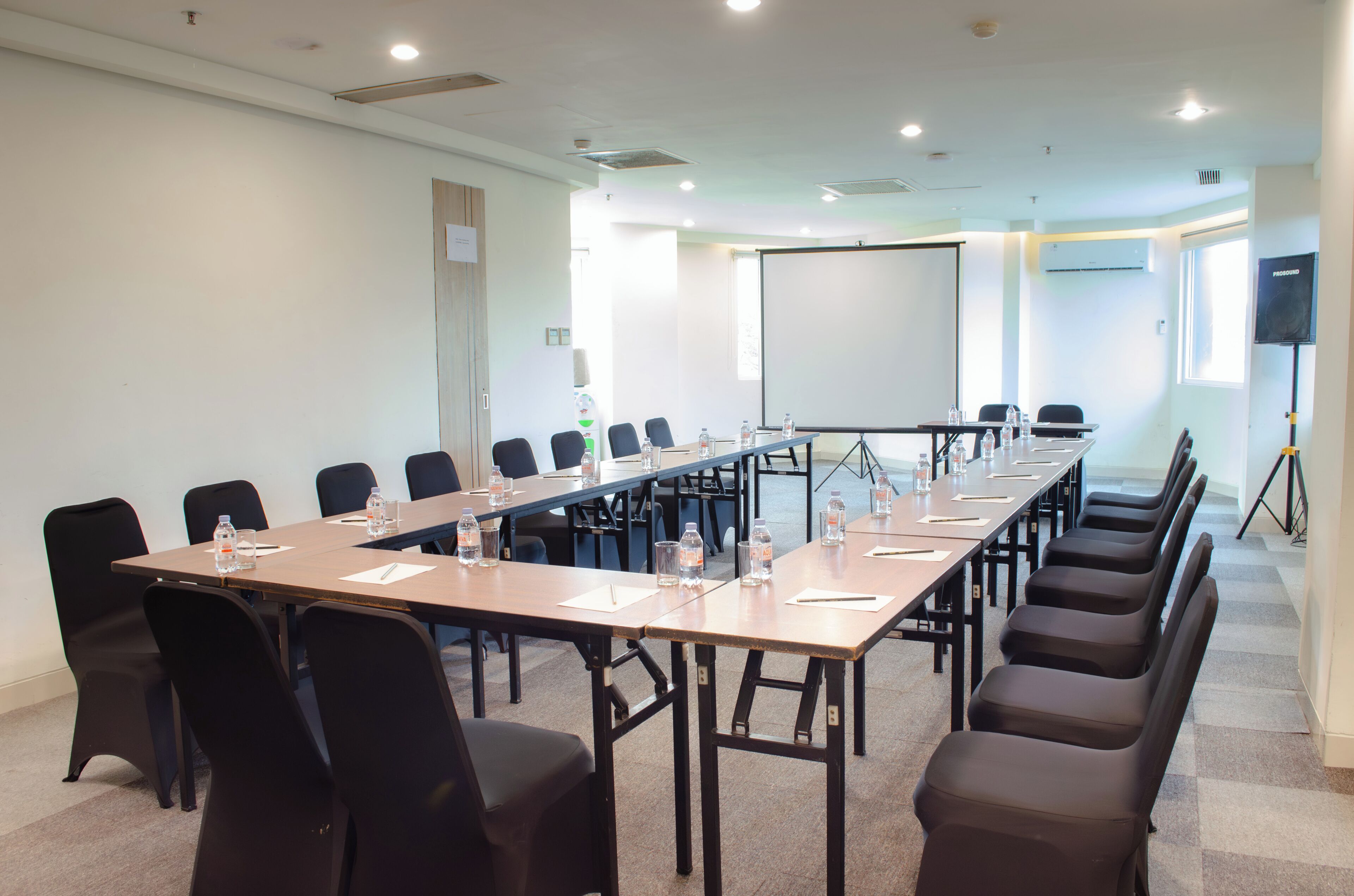 A conference room with a long table, chairs, a projector screen, and a whiteboard.