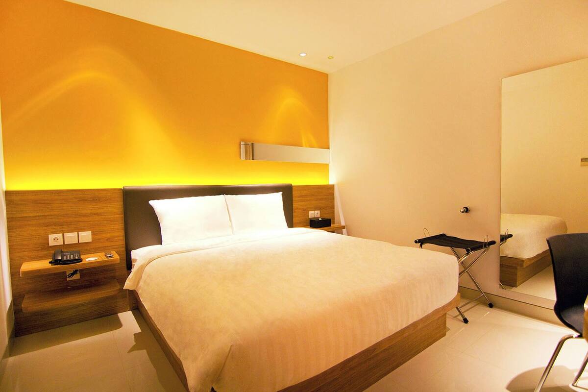 Una habitació d'hotel moderna amb un llit gran, taules de nit, escriptori i un mirall.