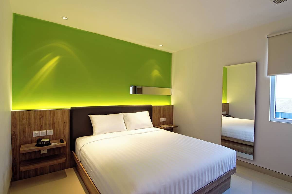 Habitació d'hotel moderna amb un llit gran, una taula de nit i un mirall, amb una paret verda decorativa.