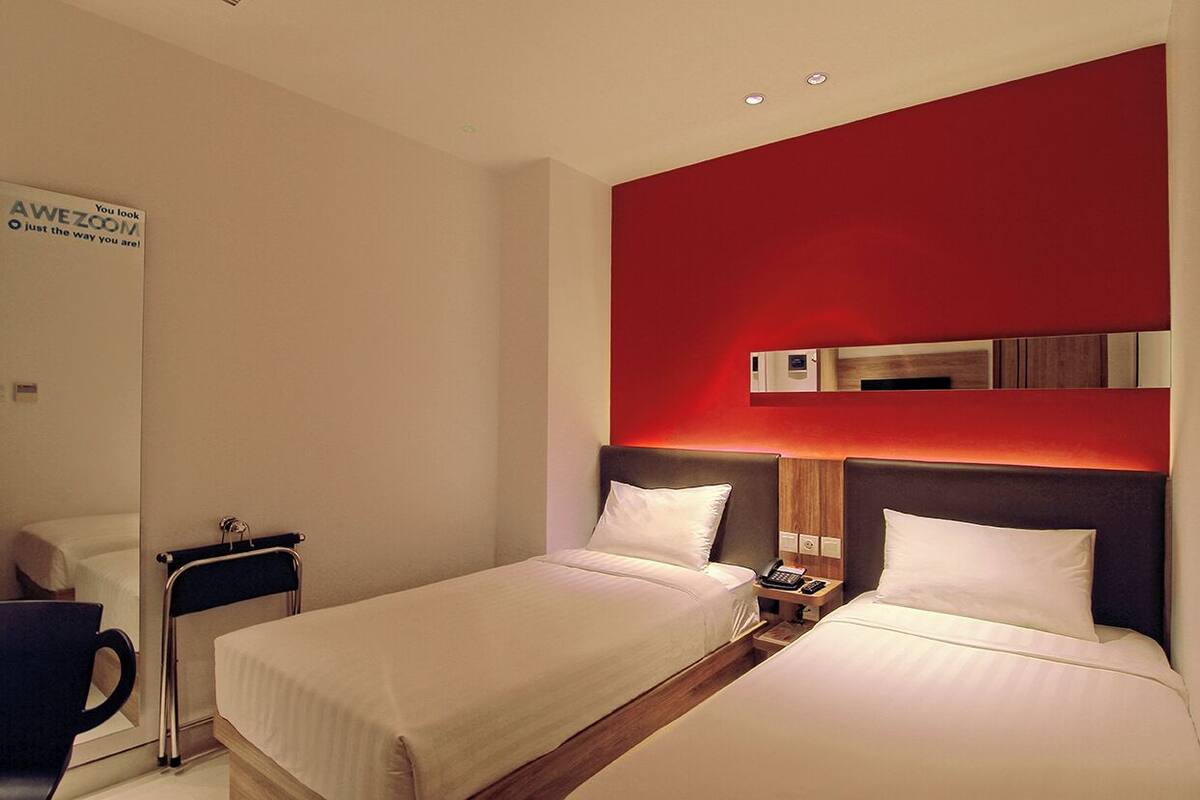 Habitació d'hotel amb dos llits, una paret d'accent vermella, un mirall i una taula de nit amb un telèfon.