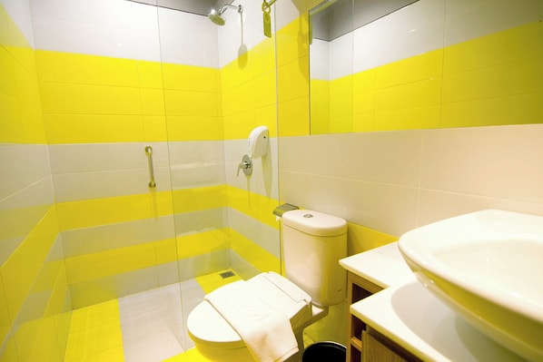 Une salle de bain avec des carreaux jaunes et blancs, des toilettes, un lavabo et un espace douche.