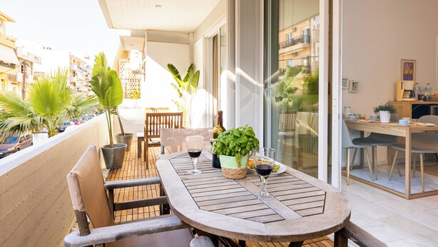 A balcony with a table, chairs, potted plants, and a dining area with a table and chairs.