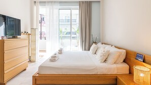 A bedroom with a wooden bed, a TV on a dresser, and a view of the outside balcony.
