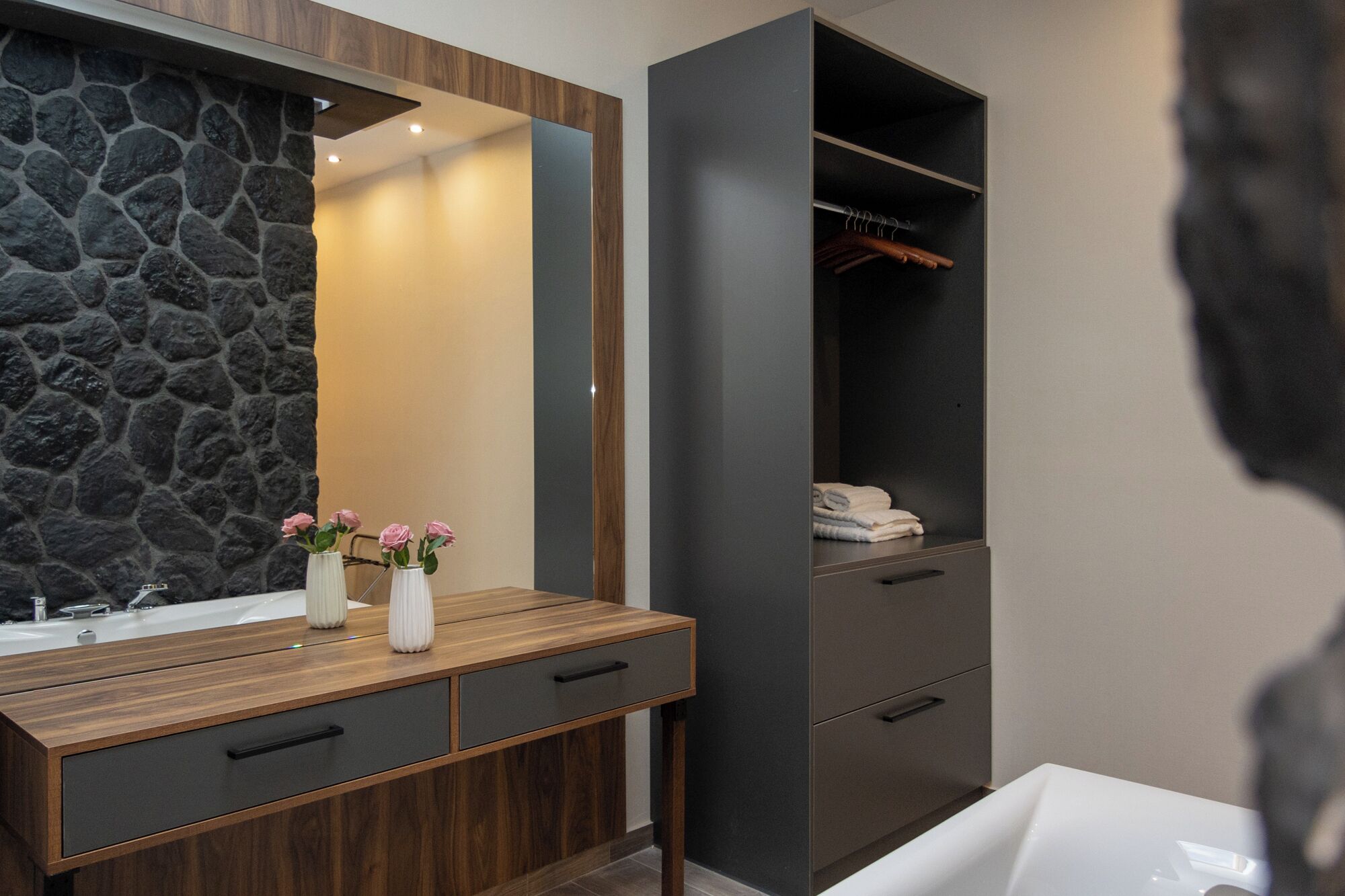 Une salle de bain moderne avec un mur en pierre, un meuble-lavabo en bois et une armoire grise.