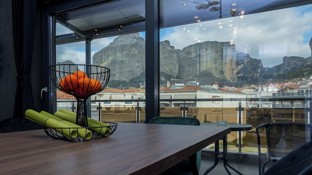 A dining area with a view of a mountainous landscape through large windows. - Dioroh Suites Meteora 302 (Kalampaka)
