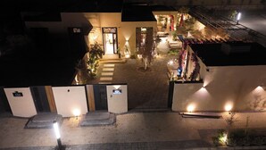 Vista nocturna de un patio de hotel con un camino central, plantas en macetas y zonas de estar al aire libre.