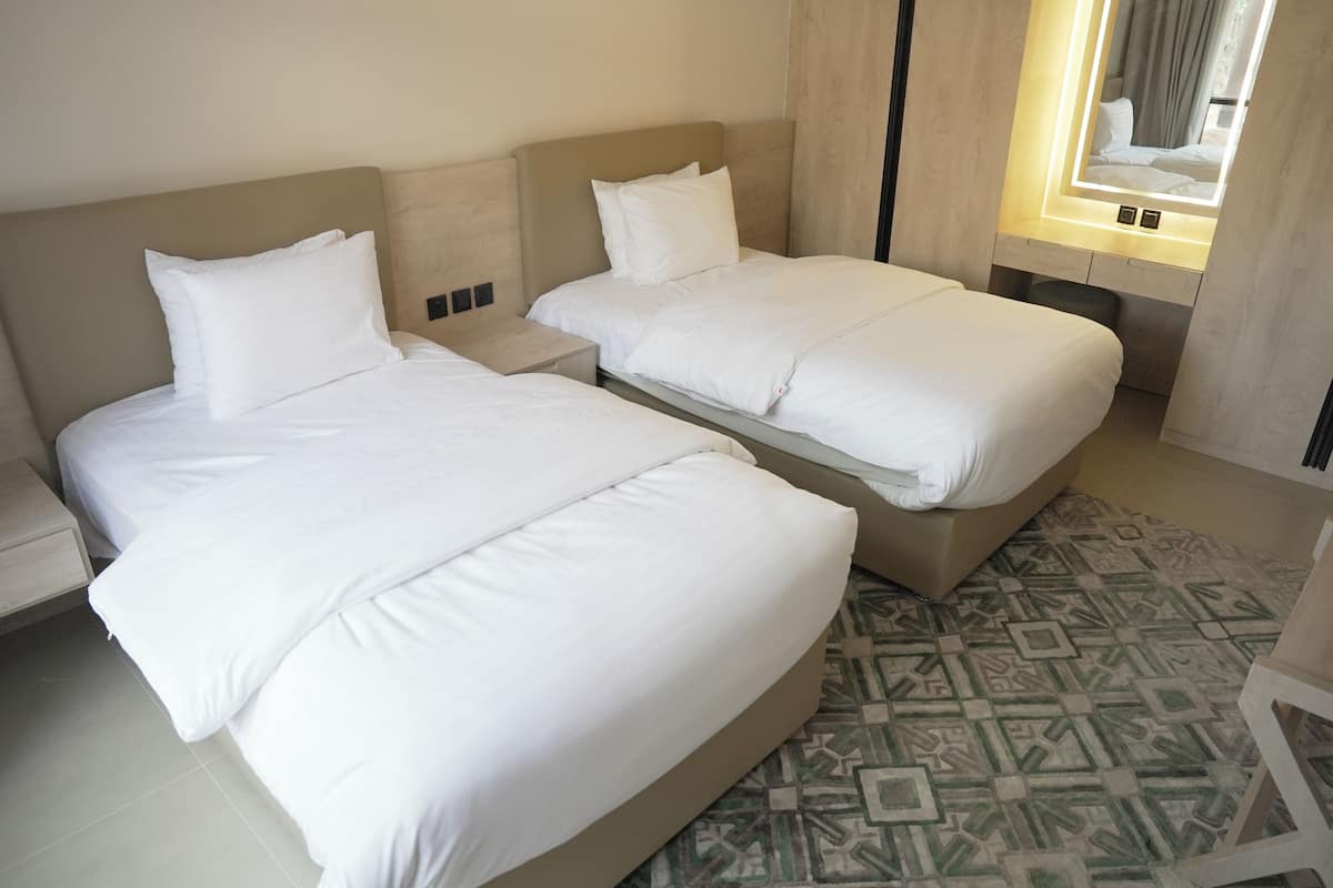 Una habitación de hotel con dos camas, una mesita de noche y un suelo estampado.