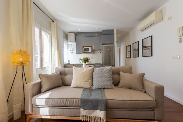 A modern living room with a sofa, a floor lamp, and a kitchen in the background.