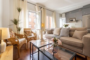 A modern living room with a sofa, two wicker chairs, a glass coffee table, and a lamp.