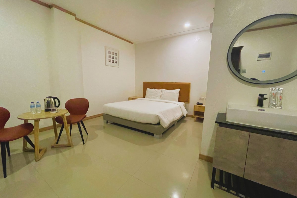 A hotel room with a bed, a round mirror, a sink, and a small table with chairs.