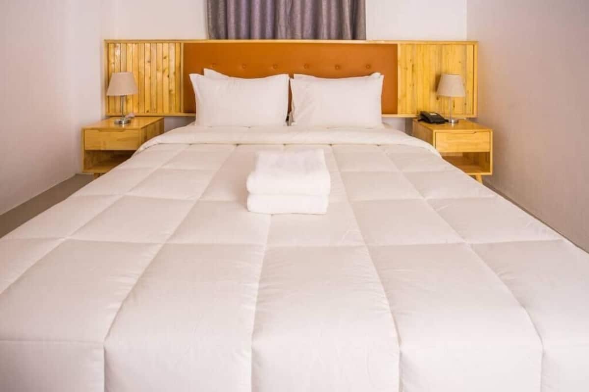 A neatly made bed with a white duvet, two pillows, and a folded white towel on the bed. There are two bedside tables with lamps and a wooden headboard.