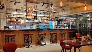 A bar area with wooden stools, a bar counter, and shelves stocked with bottles. - Hotel Halo Angeles City (Angeles City)