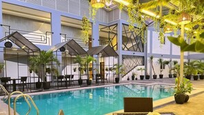 Una piscina interior con sillones y mesas, rodeada de plantas en macetas y un diseño arquitectónico moderno.