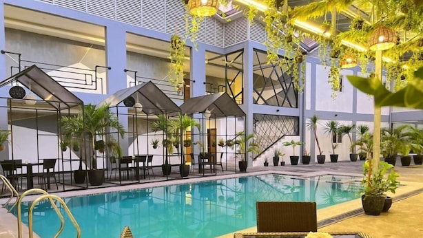 An indoor swimming pool with lounge chairs and tables, surrounded by potted plants and modern architectural design. - Hotel Halo Angeles City (Angeles City)