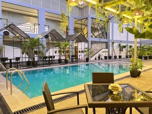 An indoor swimming pool with lounge chairs and tables, surrounded by potted plants and modern architectural design. - Hotel Halo Angeles City (Angeles City)