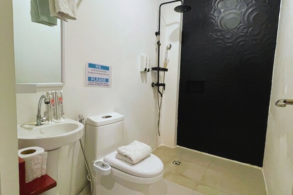 Un baño con lavamanos, inodoro y ducha. Hay un cartel en la pared y una toalla sobre el inodoro.