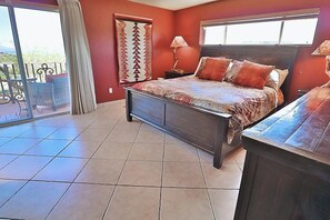 A bedroom with a bed, a nightstand, a lamp, a window, and a balcony with chairs.