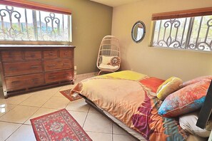 Ein Schlafzimmer mit einem Bett, einem Schminktisch, einem Stuhl und zwei Fenstern mit dekorativen Eisenverzierungen.