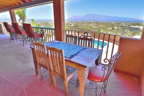 Un patio esterno coperto con tavolo e sedie, una piscina e vista su un paesaggio desertico.