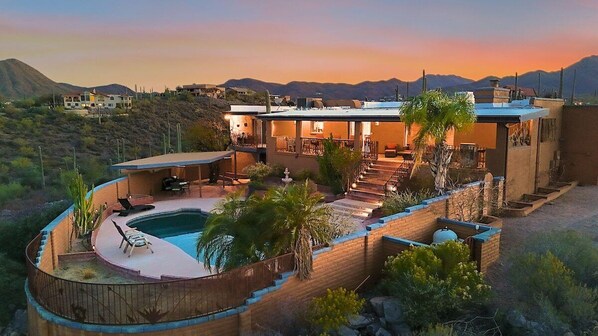 A modern house with a swimming pool, outdoor seating, and a view of the mountains.