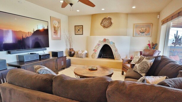 Una sala de estar con televisor de pantalla plana, chimenea, conjunto de sofá y ventilador de techo.