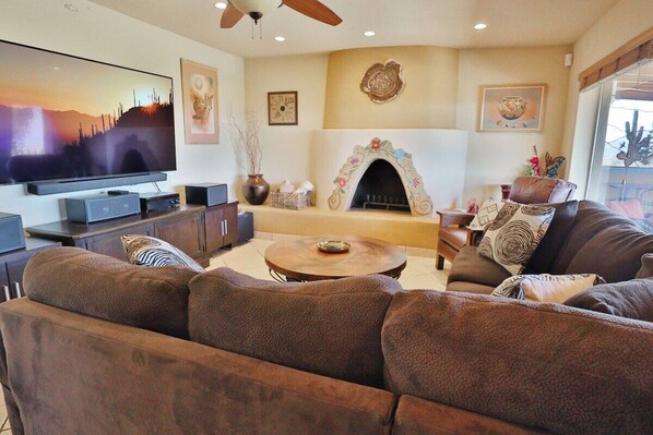 A living room with a flat-screen TV, a fireplace, a sofa set, and a ceiling fan.