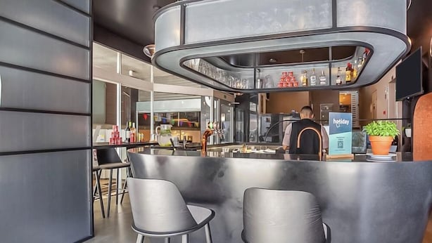 A modern bar area with stools, a counter, and a person behind the bar. - Hotiday Room Collection - Oporto (Porto)