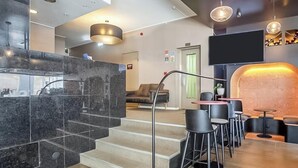 A modern hotel lobby with a marble reception desk, a staircase, and a seating area with tables and chairs. - Hotiday Room Collection - Oporto (Porto)