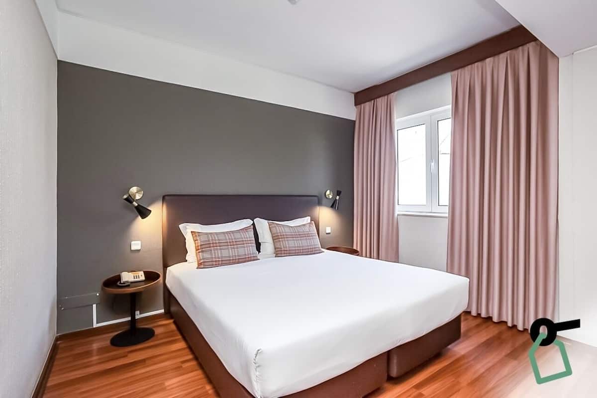 A modern hotel room with a large bed, bedside lamps, a nightstand, and a window with curtains.