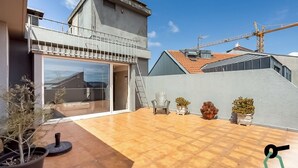 A modern house with a balcony, a garage, and a tiled patio area with potted plants.