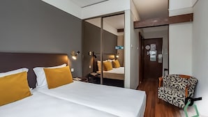 A hotel room with a large bed, a chair, a mirror, and a door leading to another room.