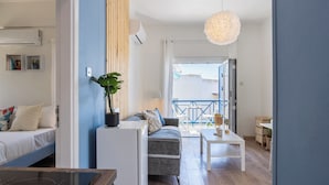 Un salon moderne avec un canapé, une table à manger et une plante en pot. On aperçoit un balcon avec une balustrade à travers l’embrasure de la porte.